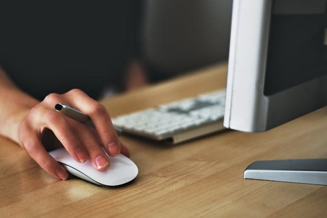 a hand of a woman sitting at a desktop computer holding a mouse