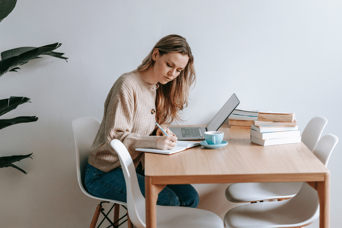 A woman sitting in front of her laptop, writing down the ideas for her next LinkedIn post.